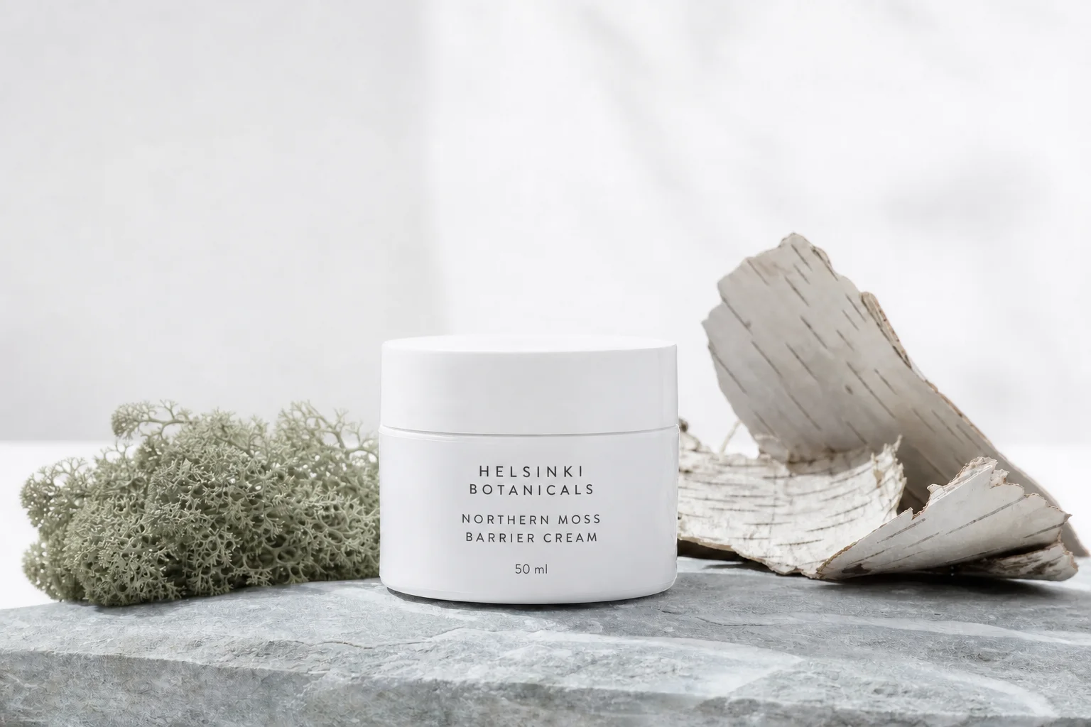 Northern Moss Barrier Cream jar beside moss and birch bark on pale stone